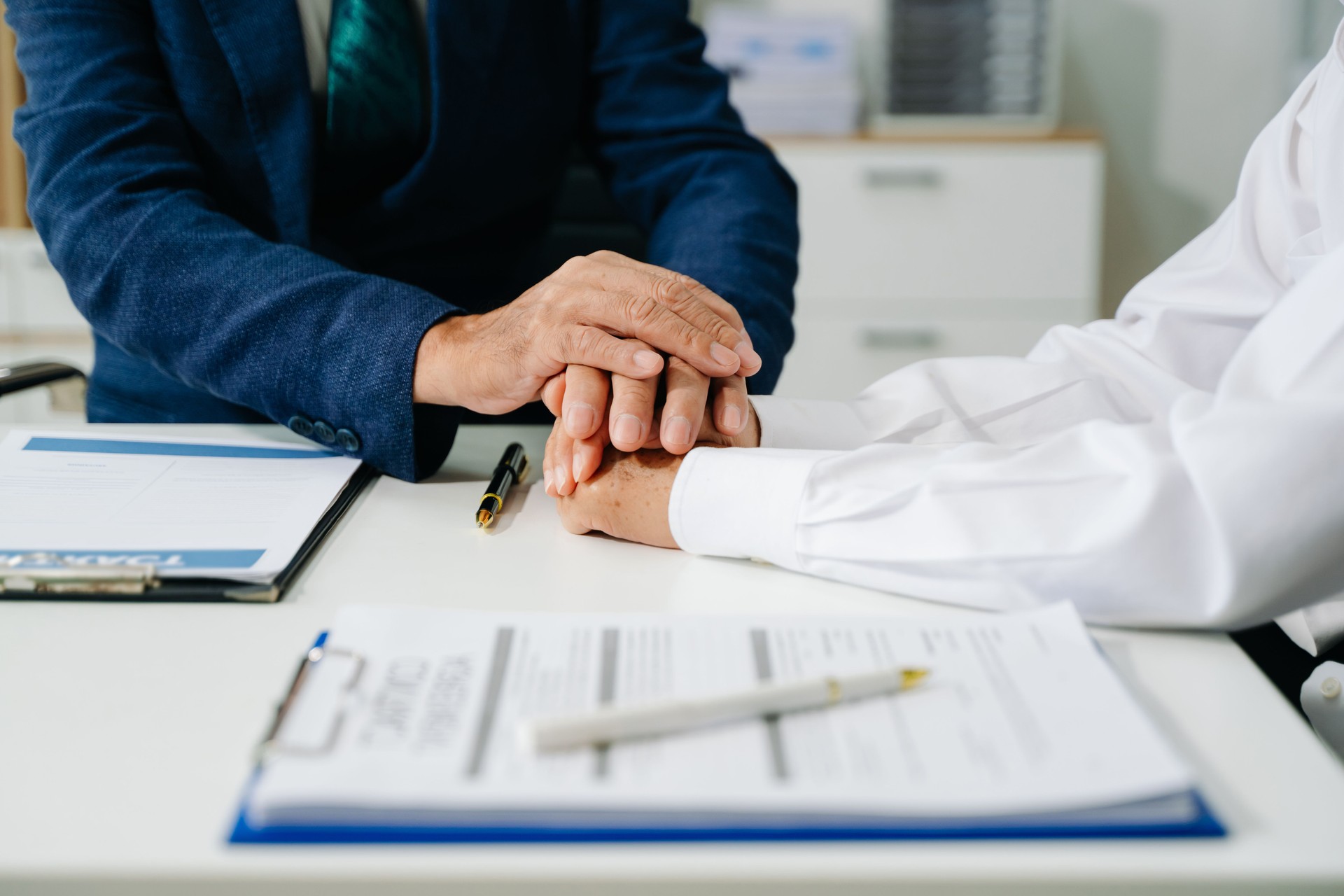 Business people compassionately holding hands and discussing contract papers with laptop and tablet